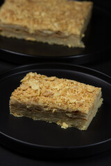 Napoleon cake on a black plate on a black background. homemade baking