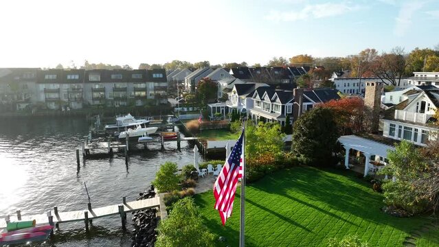 American flag at waterfront. Upscale homes with water view on sunny autumn day. Aerial orbit.