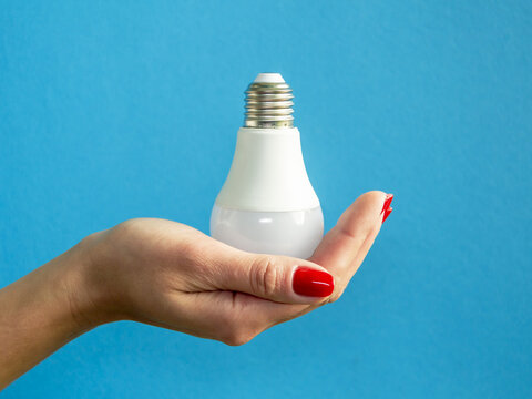 lamp in a woman's hand. female fingers holding LED lamp. idea. New idea or inspiration concept. Concept of startup. blue background. Horizontal image.