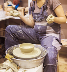 Female clay artist working on pottery wheel at ceramic studio.