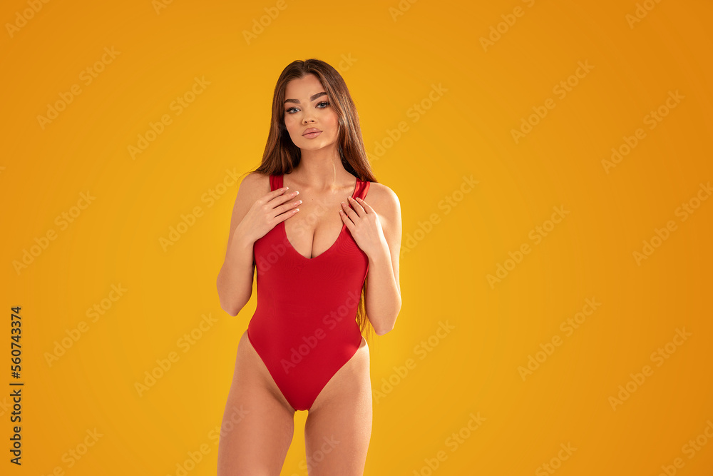 Wall mural Attractive brunette woman posing in red swimwear,  summer style. Studio yellow background.