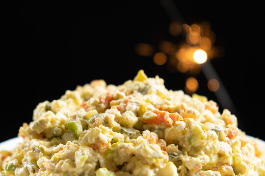 Olivier russian salad - a classic recipe with mayonnaise, an incredible taste, on a black background, with bokeh of sparklers for christmas and new year