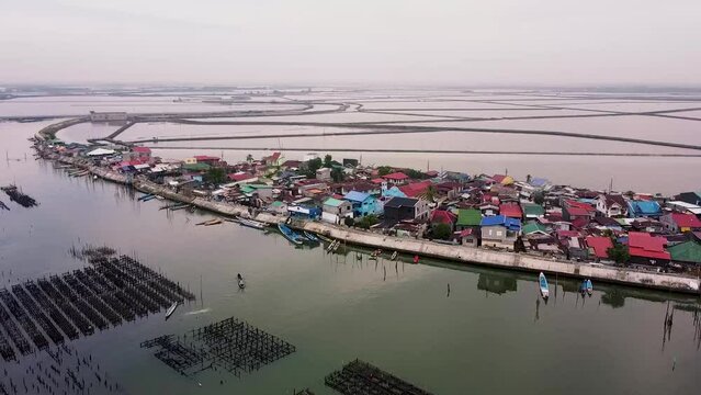 Aerial footage of fishing village in Paombong, Bulacan, Philippines. Shot on DJI Mini 2. Establishing shot of remote fishing village with houses surrounded by fishpond. Cloudy skies and vast waters.