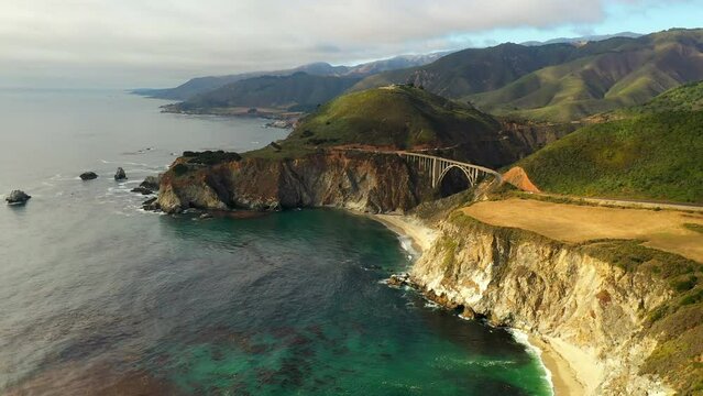 Aerial Shot Of Bixby Canyon Bridge At Beach Under Clouds, Drone Flying Backwards Over Sea - San Francisco, California