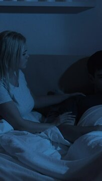 Night couple problem. Sexual dysfunction. Supportive wife cheering up depressed disappointed ashamed sad husband in bed late in dark bedroom. Vertical video.