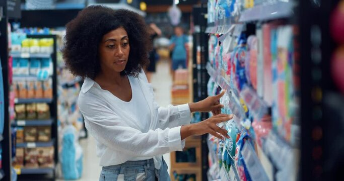 Multi-ethnic dark-skinned beautiful woman housewife compares price tags while shopping for the phosphate-free washing powder on shelves in the household chemicals department of a supermarket.