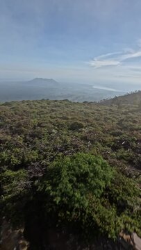 Tropical island volcano crater stone texture with greenery bushes nature sea landscape fog aerial view. FPV sports drone low shot extreme man running on mountain ridge Asian scenery. Vertical video 4k