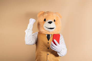 Person wearing a teddy bear mask on a yellow background raises her arm in victory symbol while consulting her smartphone.