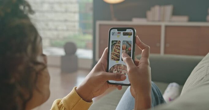 Woman food online sitting at couch. Close up female hand scrolling through menu on the internet. Person ordering lunch from home