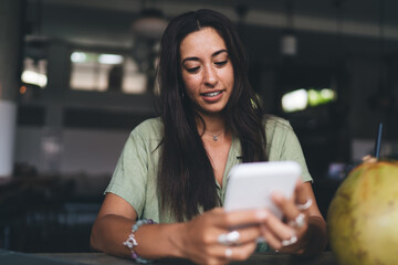 Cheerful woman using cellphone while having refreshing drink
