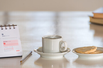 close up of coffee cup with smoke, a diary and books, a pen to write with, behind a luminous window