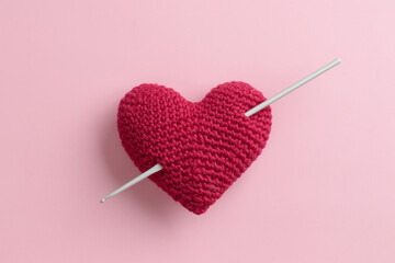 Crocheted amigurumi purple red burgundy heart with crochet hook on a pink background. Valentine's day banner
