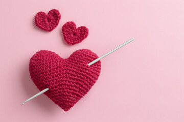 Crocheted amigurumi pink heart with a hook on a pastel pink background. Valentine's day gift banner...