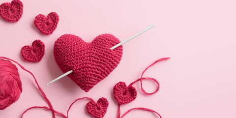 Crocheted amigurumi purple red burgundy hearts with crochet hook on a pink background. Valentine's day banner