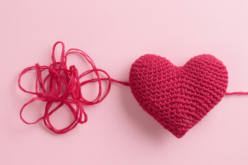 Crocheted amigurumi pink heart with a yarn on a pastel pink background. Valentine's day gift banner with a copy space, health conception of handmade