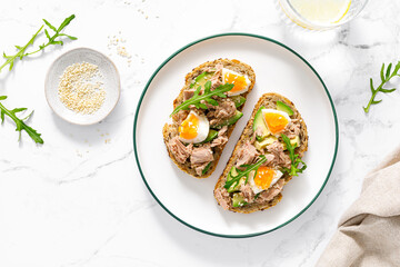 Tuna toast. Open sandwiches with whole grain bread, canned tuna, boiled egg, avocado and arugula. Top view