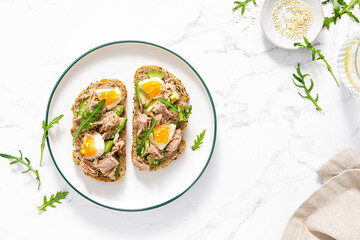 Tuna toast. Open sandwiches with whole grain bread, canned tuna, boiled egg, avocado and arugula. Top view