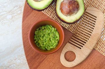 Fresh avocado puree in a small clay bowl and wooden hairbrush. Homemade face mask, natural beauty treatment and spa recipe. Top view, copy space.