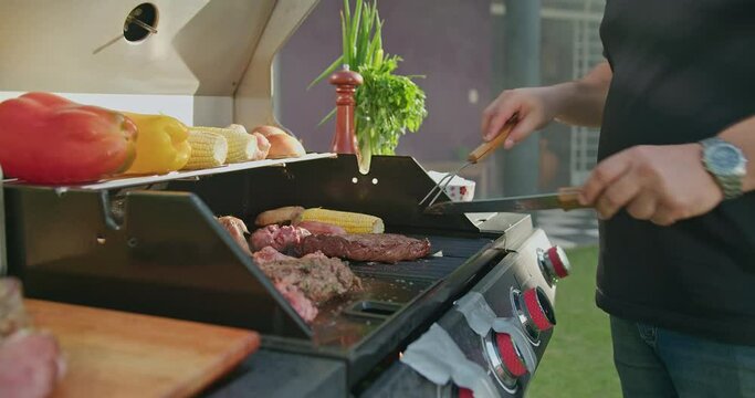 Happy chef preparing meat on grill at home barbecue party. Person grilling juicy steak