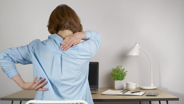 Pain in the back and neck of a woman from fatigue at work on a laptop in the office.