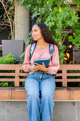 Smiling black student woman sitting and waiting for a classmate outside the mall. Education concept