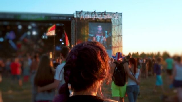 Woman running to stage. Diverse group of fans dancing at openair live rock concert. Asian woman slam at music festival outdoor. Rebellious young anarchist people listening to alternative punk songs