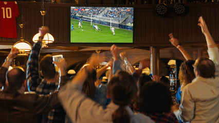 Fototapeta Group of Soccer Fans Cheering, Screaming, Raising Hands and Jumping During a Football Game Live Broadcast in a Sports Pub. Player in Blue Shirt Scores a Goal and Friends Celebrate. Slow Motion Footage obraz