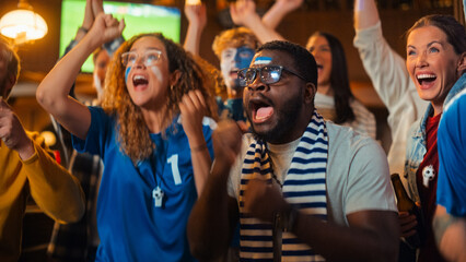 Fototapeta premium Group of Multiethnic Friends Watching a Live Soccer Match on TV in a Sports Bar. Fans with Painted Faces Cheering. Young People Celebrating When Team Scores a Goal and Wins the Football World Cup.