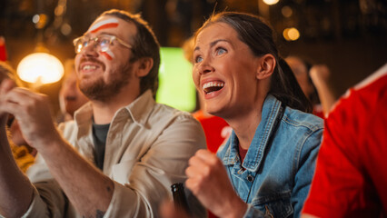 Young Soccer Fans Couple Watching a Live Football Match in a Sports Bar. Crowd with Colored Faces Cheering for Their Team. Player Scores a Goal and Crowd Celebrate Winning the Championship.