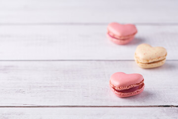 Three heart shaped, cream filled French Macaroons on white wooden Background. Traditional confectionery for Valentine's Day, Mother's Day, Wedding or romantic Love. Closeup with pastel colors.