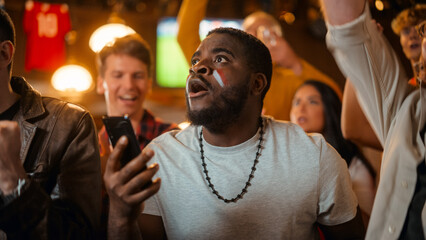 Portrait of an Excited Young Black Man Holding a Smartphone, Anxious About a Sports Bet on His Favorite Soccer Team. Lively Successful Emotions When Football Team Scores a Winning Goal.