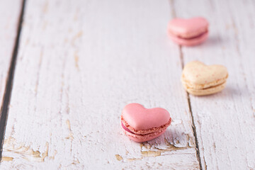Three heart shaped, cream filled French Macaroons on white wooden Background. Traditional confectionery for Valentine's Day, Mother's Day, Wedding or romantic Love. Closeup with pastel colors.