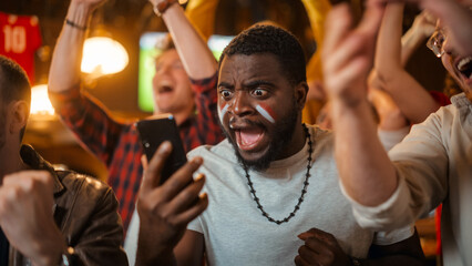 Portrait of an Excited Young Black Man Holding a Smartphone, Anxious About a Sports Bet on His...
