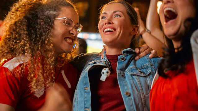 Three Female Friends Watching a Live Soccer Match on TV in a Sports Bar. Happy Girls Cheering and Shouting. Young Fans Celebrating When Team Scores a Goal and Wins the Football World Cup. - Powered by Adobe
