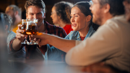 Male and Female Friends Sitting at Bar Counter, Cheering and Toasting with Beer Glasses, Enjoying...