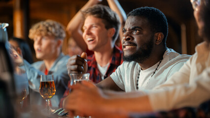 Nervous African Man Watching a Live Soccer Match on TV in a Sports Bar. Excited Fans Cheering and...