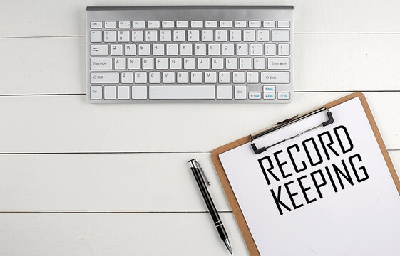 Home office workspace with keyboard, clipboard and pen with text RECORD KEEPING on white wooden background , business concept