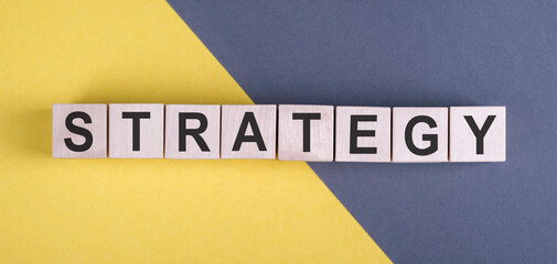 Obraz premium STRATEGY word written on wood blocks on yellow and gray background