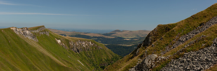 Panoramic green mid-mountain landscape under the sun without trees. Panoramic view of the valley under the sun with a blue sky.
