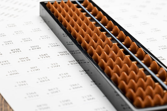 Japanese abacus soroban composed of an odd number of columns or rods, each having beads. It is placed on printed practice sheet for calculations of addition and multiplication 