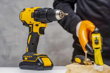 Male worker holds a close-up electric cordless screwdriver in his hands against the background of a construction tool and a concrete wall.