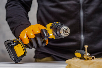 Male worker holds a close-up electric cordless screwdriver in his hands against the background of a...