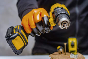 Male worker holds a close-up electric cordless screwdriver in his hands against the background of a construction tool and a concrete wall.