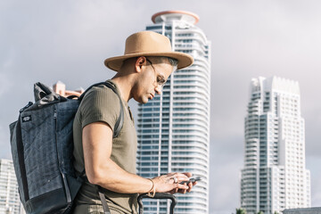 Close up, profile of traveller man with a brown hat, looking for direction on his smartphone.