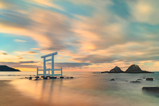Long exposure art photography of a sunset seascape depicting the Itoshima Beach of Fukuoka famous for its white Shinto torii gate in front of the Couple Rocks called Sakurai Futamigaura's Meoto Iwa.
