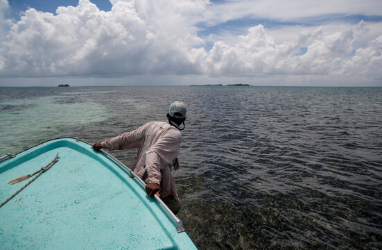 man wades in shallow ocean pulling bow of flats boat through water