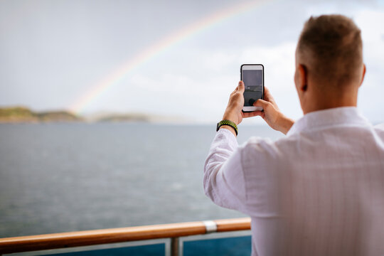 Man on ship photographing rainbow with smartphone, Norway