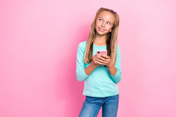 Portrait of minded cheerful girl hold telephone look interested empty space isolated on pink color background