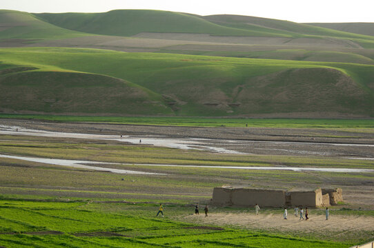 Boys play soccer on a bare patch of ground, beside a river and below hills brushed with spring green, in the district headquarte