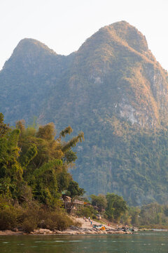 Hotel on shore of Nam Ou river in front of tall forest cliff, Muang Ngoi, Phongsaly, Laos